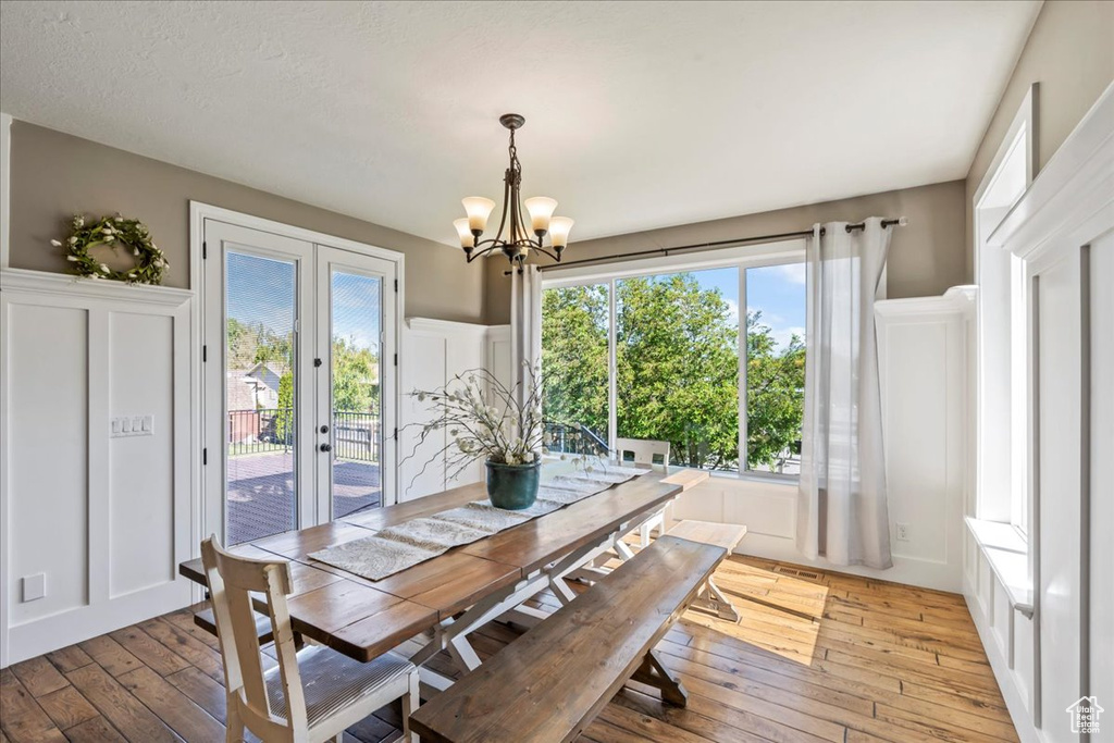 Dining space with light wood-type flooring, a chandelier, a decorative wall, french doors, and wainscoting