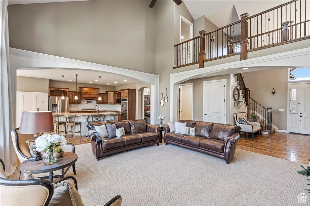Living area with arched walkways, a high ceiling, stairs, wood finished floors, and baseboards
