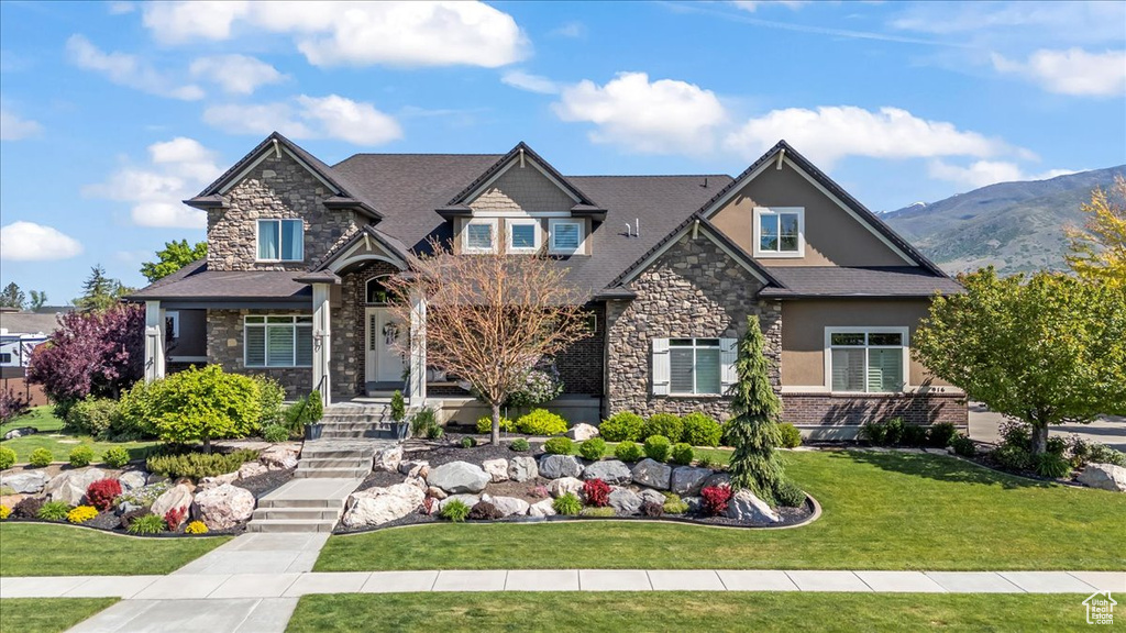 Craftsman house featuring stone siding, a front yard, stucco siding, a mountain view, and roof with shingles