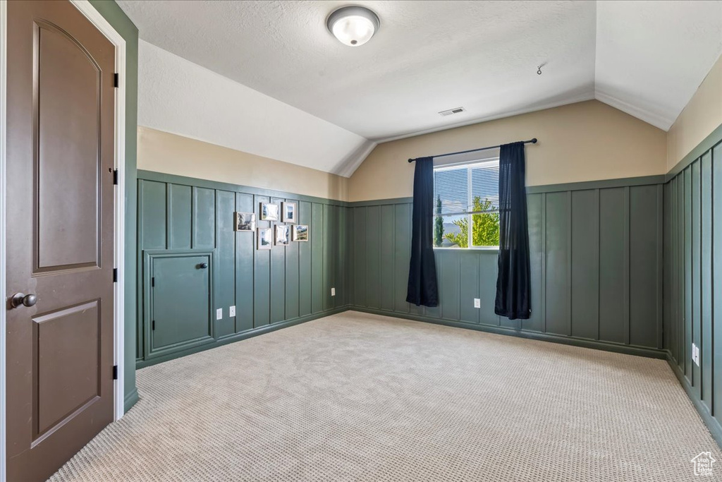 Additional living space with lofted ceiling, light carpet, a decorative wall, a wainscoted wall, and a textured ceiling