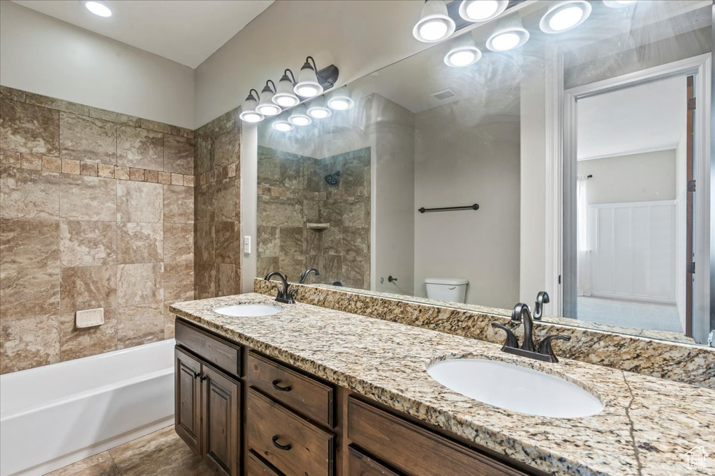 Full bathroom with toilet, double vanity, and shower / bath combination