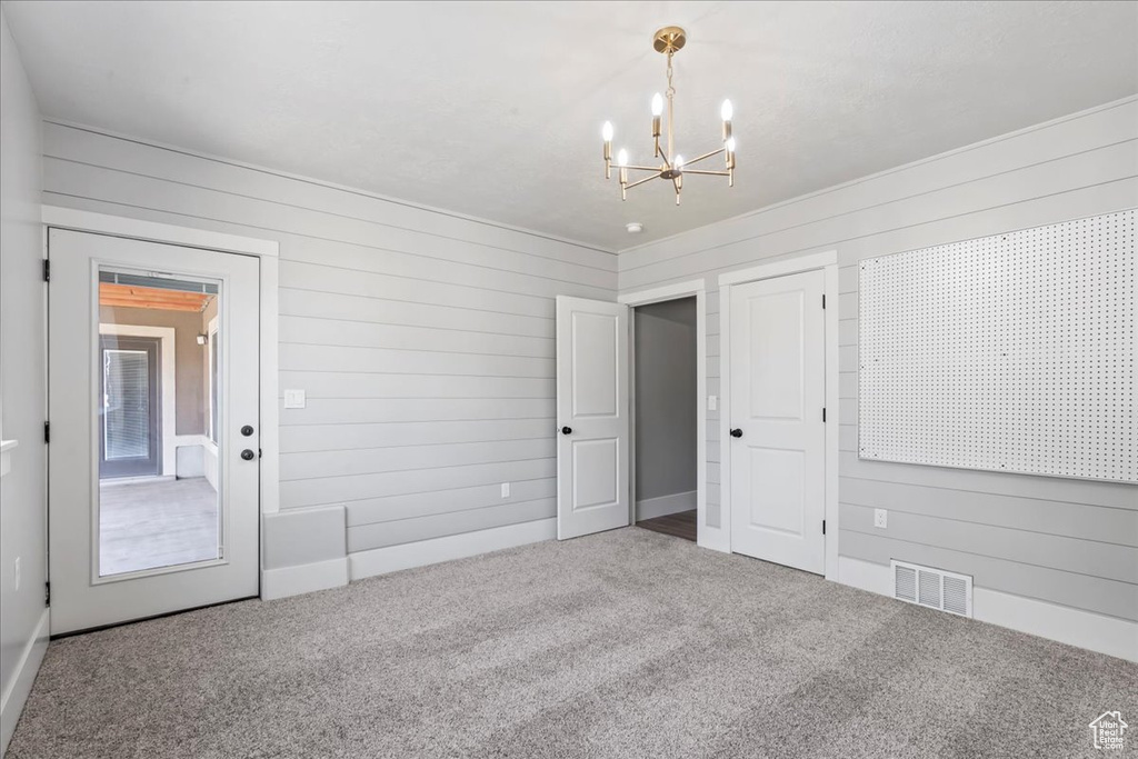 Carpeted empty room featuring wooden walls and a chandelier