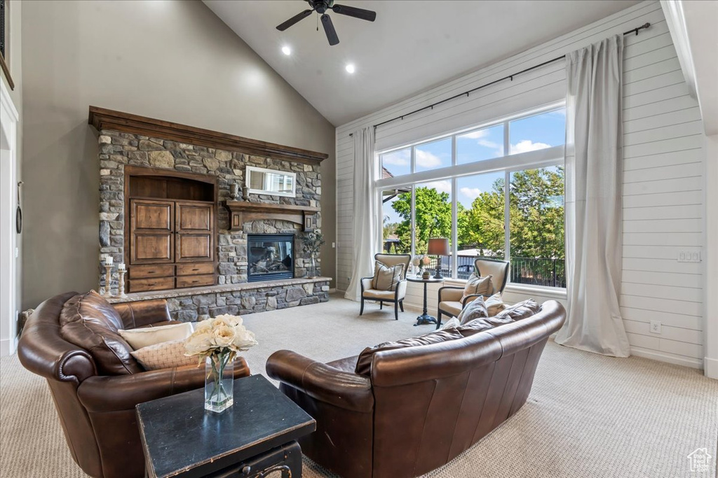 Living room with carpet, a ceiling fan, high vaulted ceiling, a stone fireplace, and baseboards