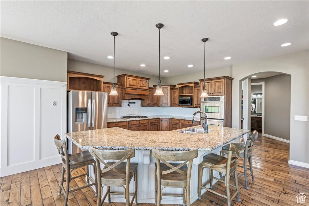 Kitchen with appliances with stainless steel finishes, a sink, arched walkways, brown cabinets, and open shelves