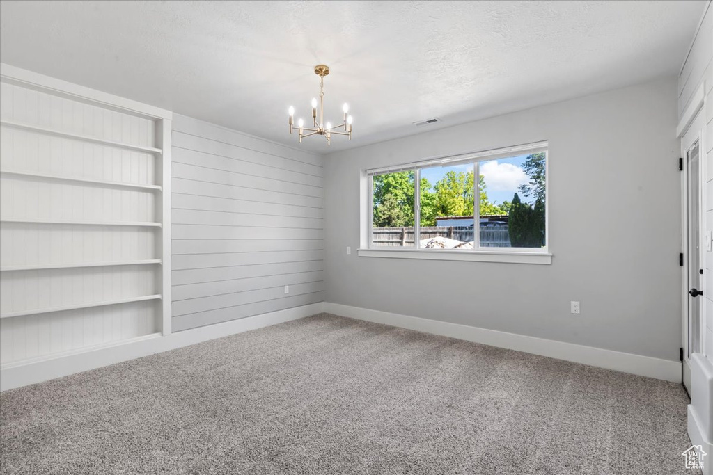 Unfurnished room featuring a chandelier, carpet flooring, and baseboards