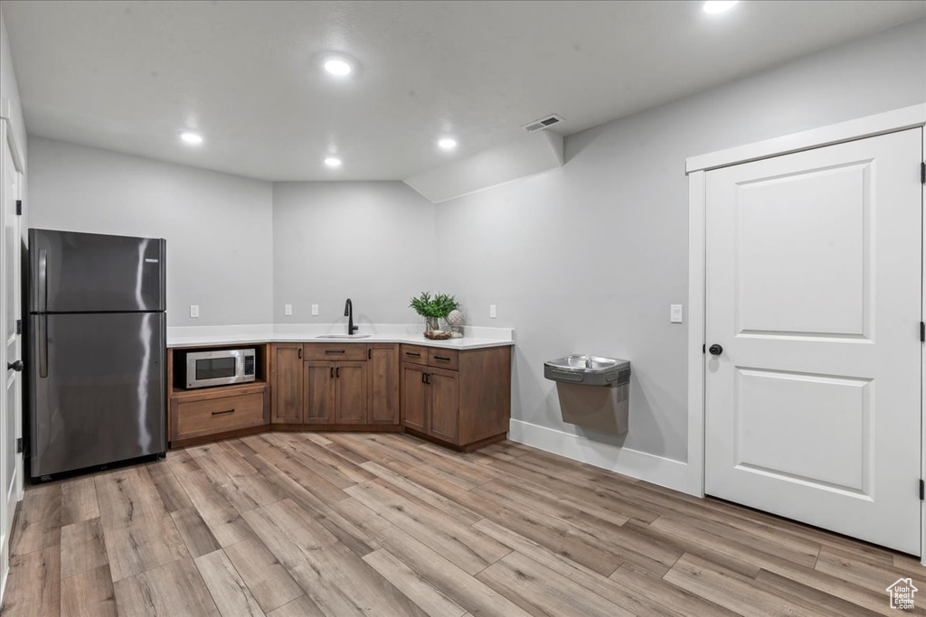 Kitchen with freestanding refrigerator, stainless steel microwave, a sink, light wood finished floors, and light countertops