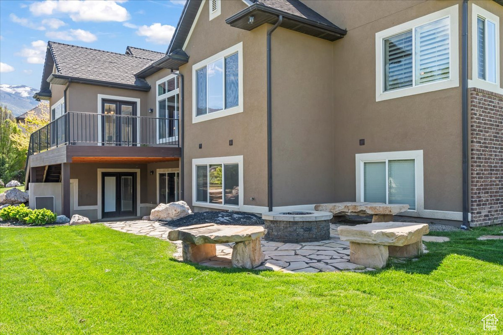 Back of house featuring a balcony, stucco siding, an outdoor fire pit, and a yard