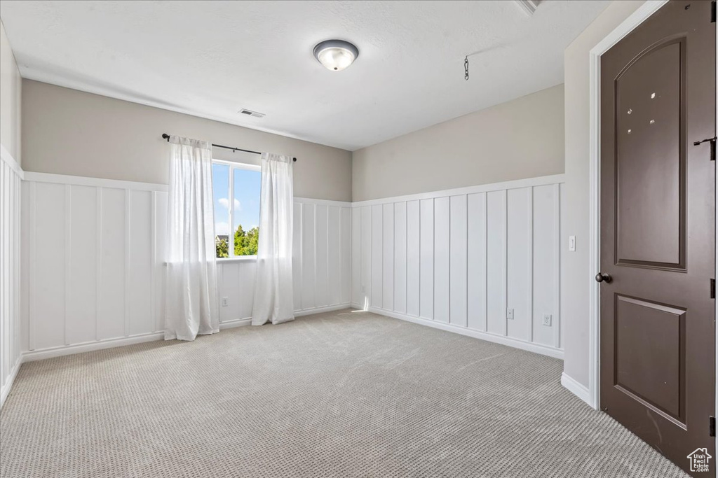 Unfurnished room featuring carpet, a decorative wall, and a wainscoted wall
