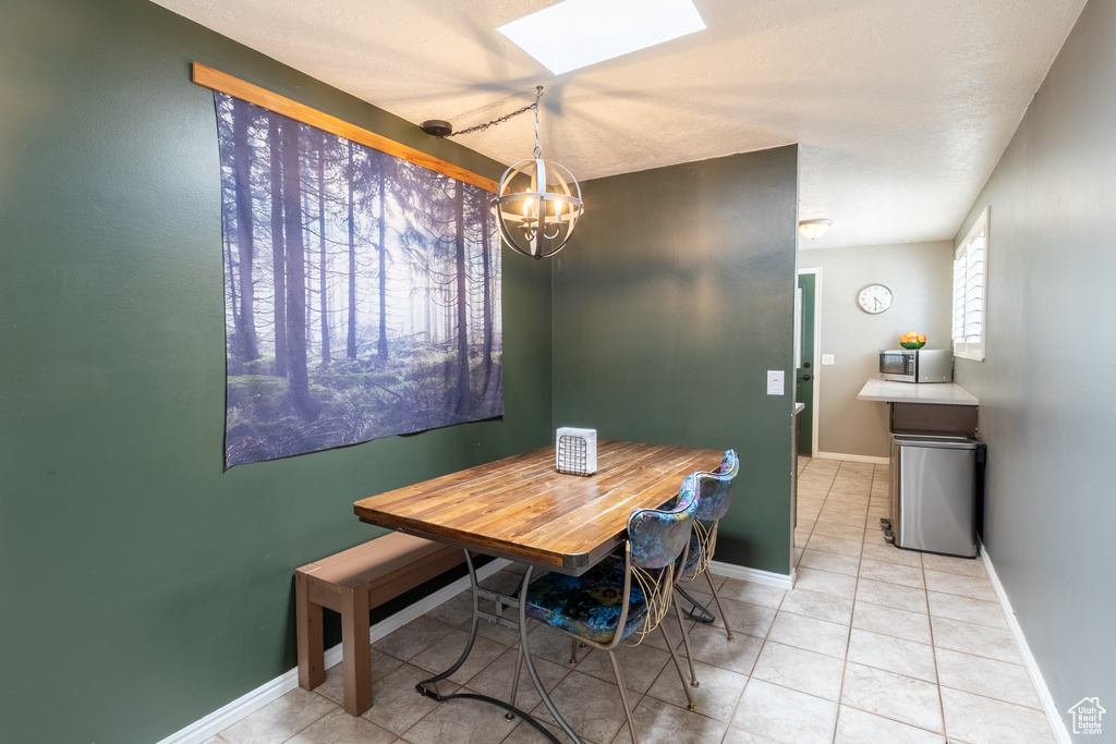 Dining area with a skylight, a chandelier, light tile patterned floors, and baseboards