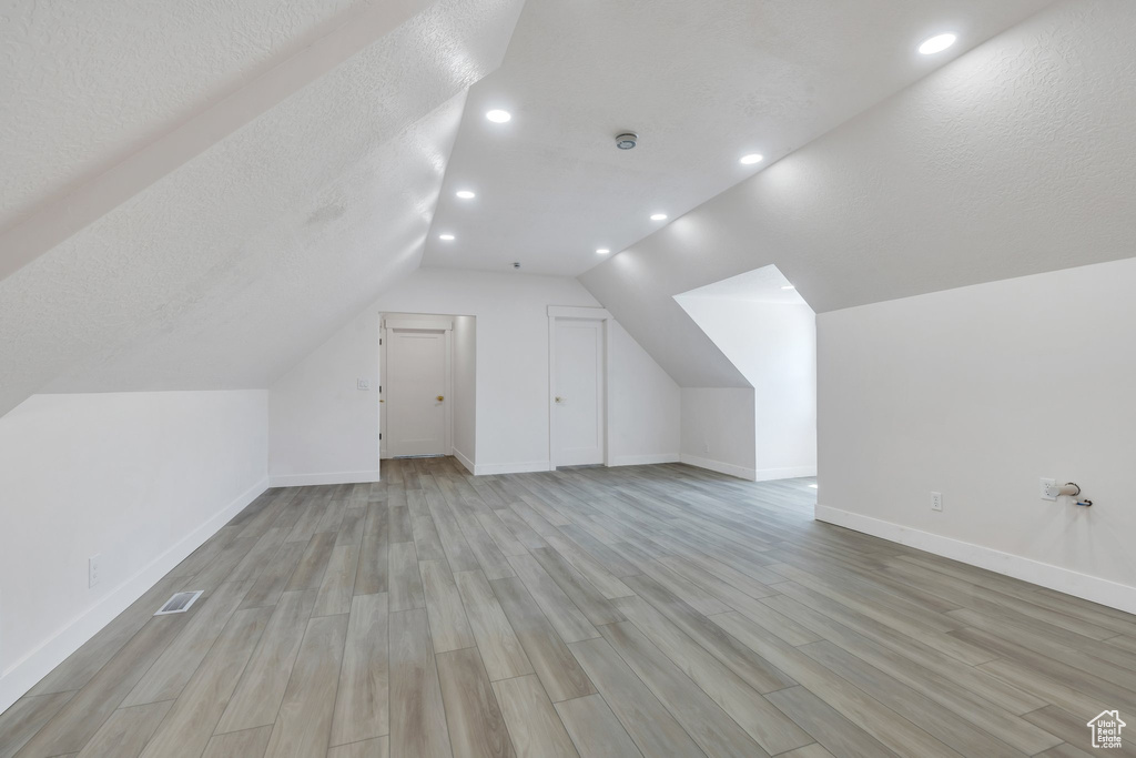 Bonus room featuring light wood-style flooring, baseboards, vaulted ceiling, recessed lighting, and a textured ceiling