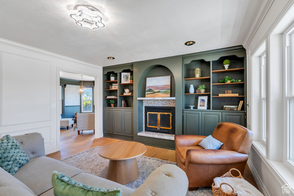 Living area featuring ornamental molding, a tiled fireplace, light wood-type flooring, and built in shelves