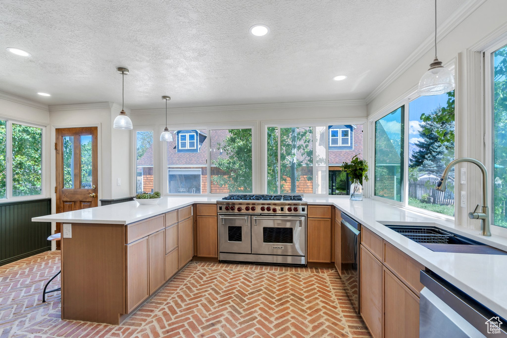 Kitchen with appliances with stainless steel finishes, a sink, brick flooring, light countertops, and a peninsula