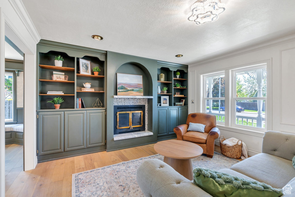 Living area featuring a tile fireplace, healthy amount of natural light, crown molding, light wood finished floors, and a textured ceiling