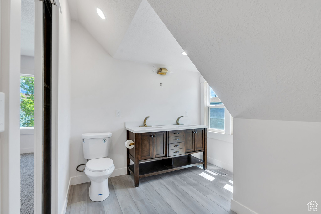 Bathroom featuring baseboards, vaulted ceiling, wood finished floors, plenty of natural light, and toilet