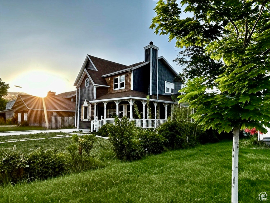Back of house featuring covered porch, a lawn, and a chimney