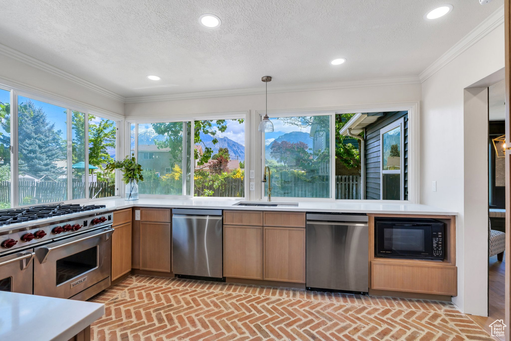 Kitchen with stainless steel appliances, a sink, brick floors, light countertops, and healthy amount of natural light