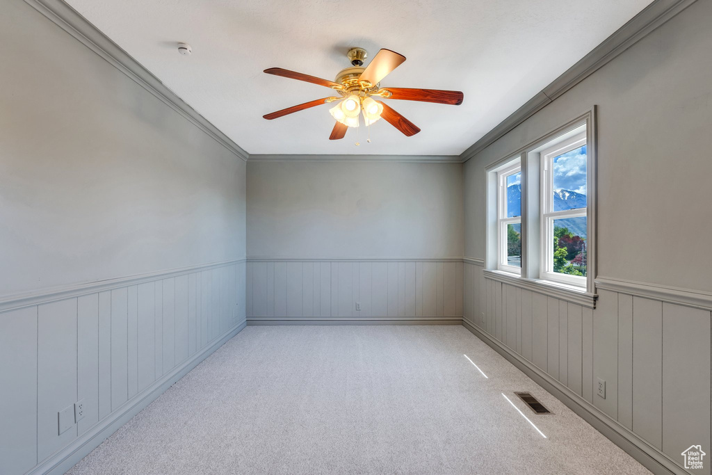 Empty room featuring ornamental molding, a ceiling fan, a wainscoted wall, and carpet floors