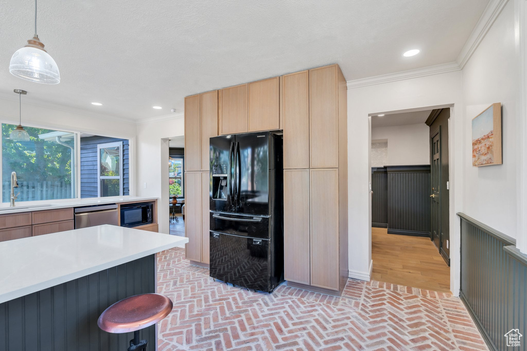 Kitchen featuring black appliances, a sink, light brown cabinetry, brick floors, and ornamental molding