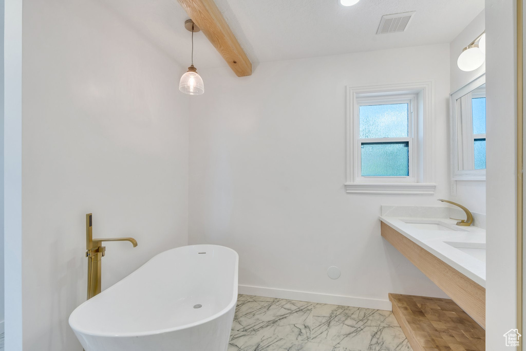 Bathroom with a freestanding bath, marble look tiles, beamed ceiling, baseboards, and double vanity