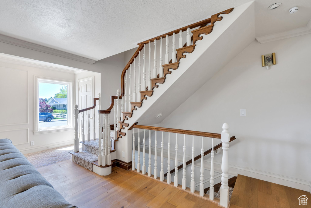 Staircase with wood finished floors, baseboards, ornamental molding, and a textured ceiling