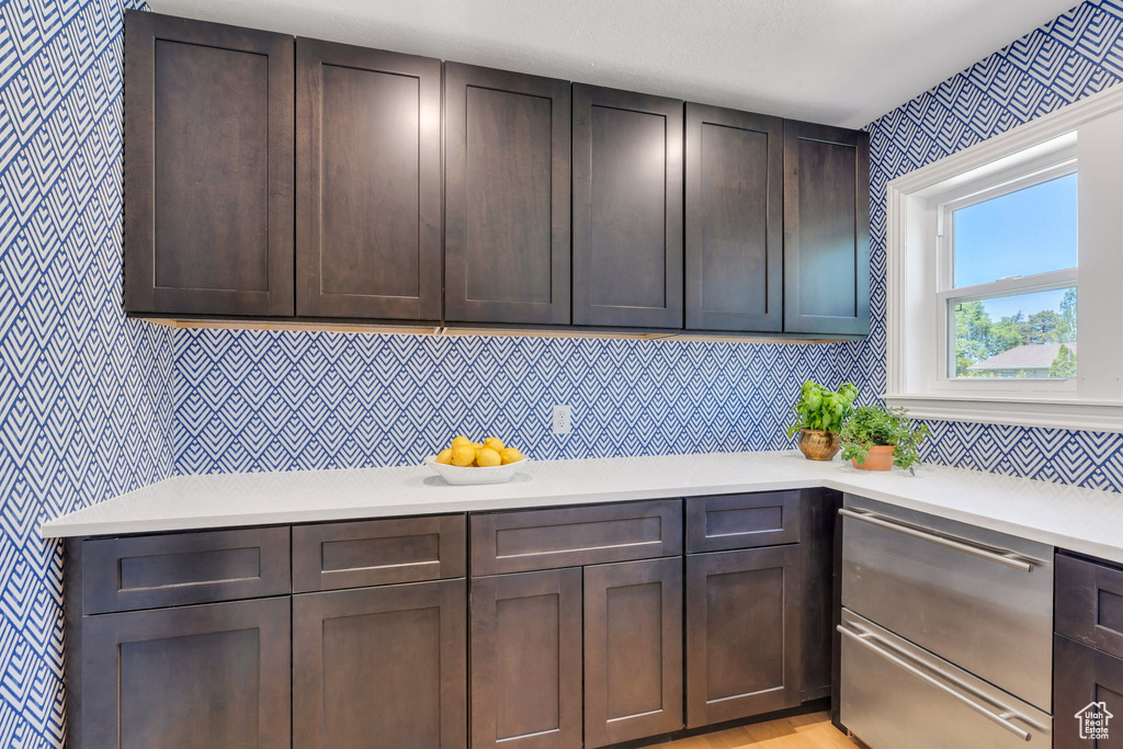 Kitchen featuring wallpapered walls, light countertops, and dark brown cabinets