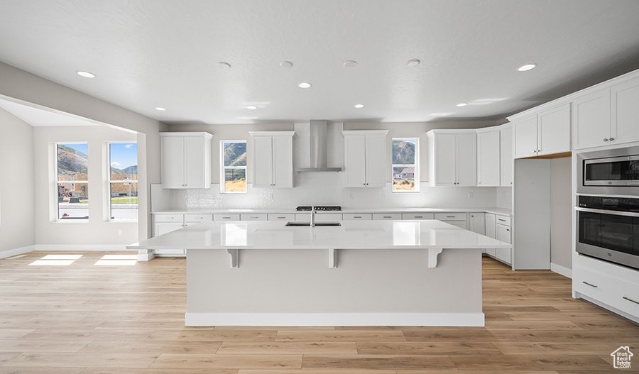 Kitchen with wall chimney exhaust hood, appliances with stainless steel finishes, recessed lighting, a kitchen breakfast bar, and light countertops