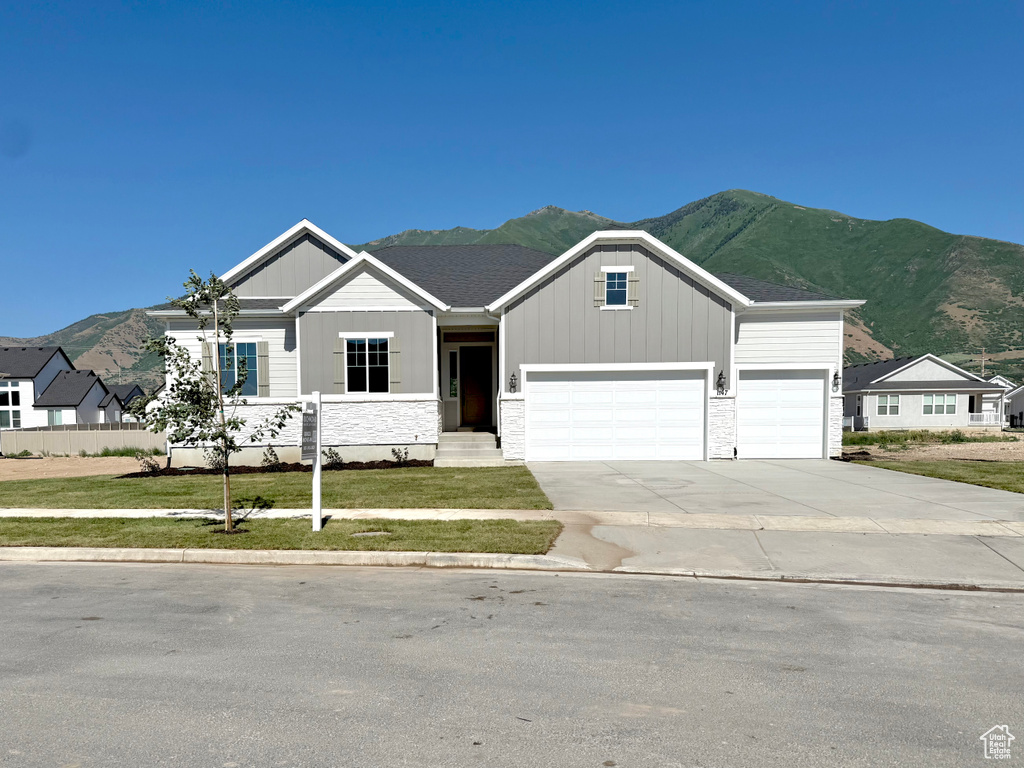 View of front of home with a mountain view, board and batten siding, an attached garage, and a front lawn