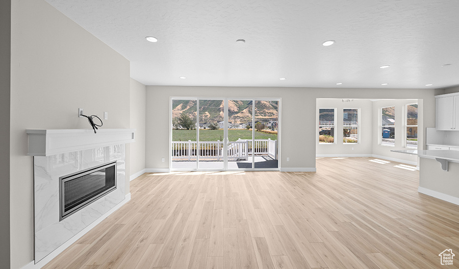 Unfurnished living room featuring light wood finished floors, a premium fireplace, baseboards, and recessed lighting