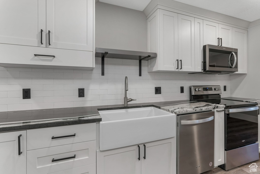 Kitchen featuring appliances with stainless steel finishes, a sink, backsplash, and white cabinets