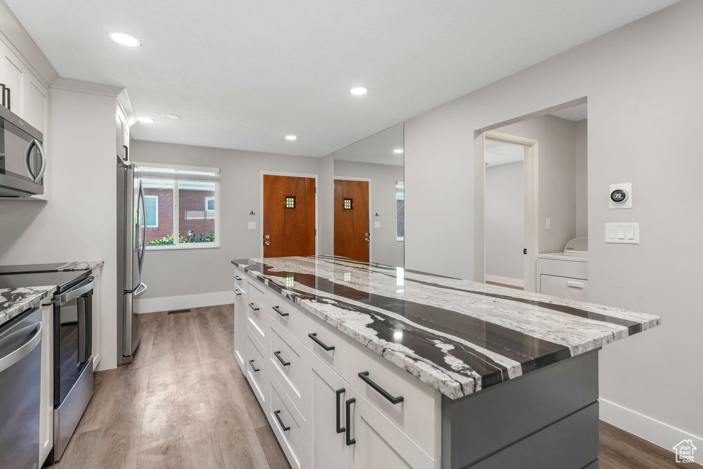 Kitchen with stainless steel appliances, light wood finished floors, baseboards, a kitchen island, and recessed lighting