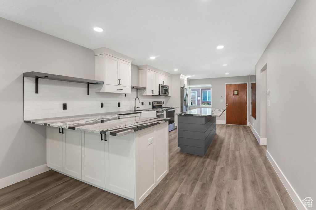 Kitchen with appliances with stainless steel finishes, wood finished floors, white cabinetry, open shelves, and baseboards