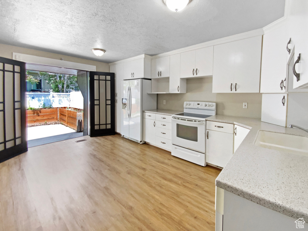 Kitchen featuring white appliances, a sink, light wood finished floors, white cabinets, and a textured ceiling