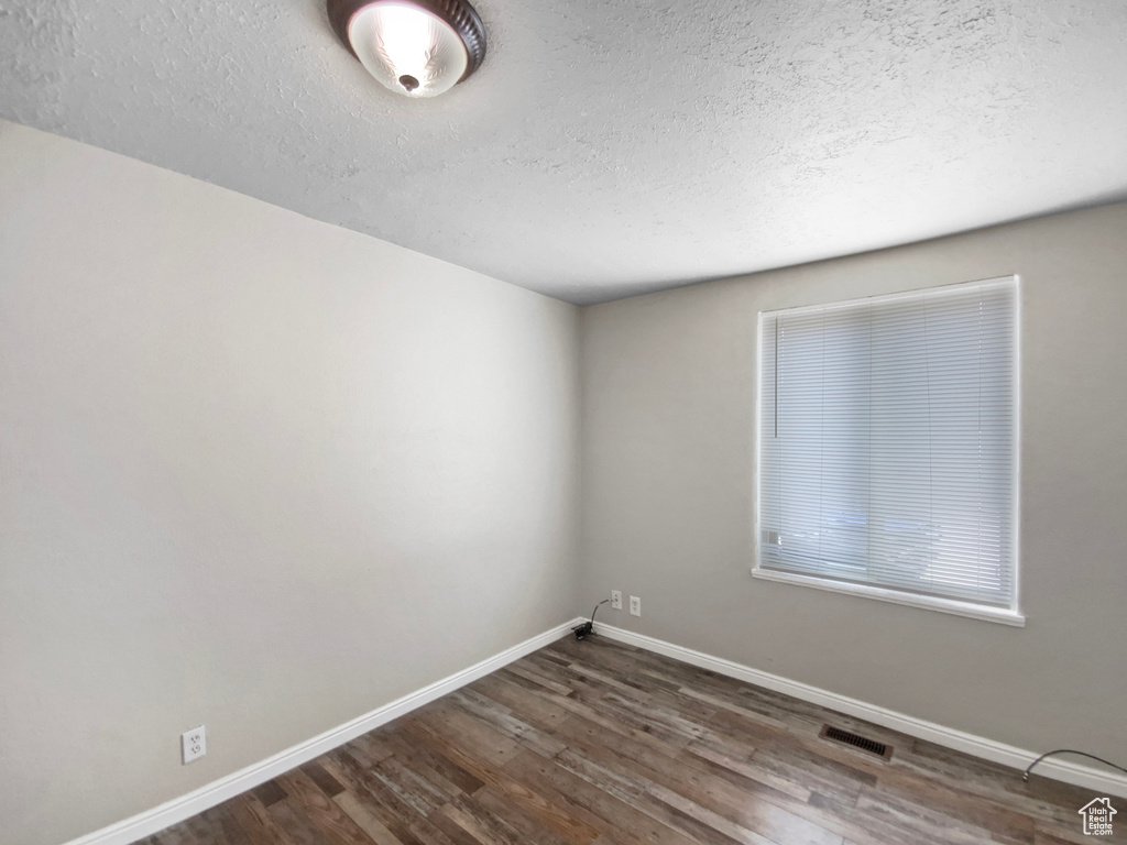 Empty room with wood finished floors, a textured ceiling, and baseboards
