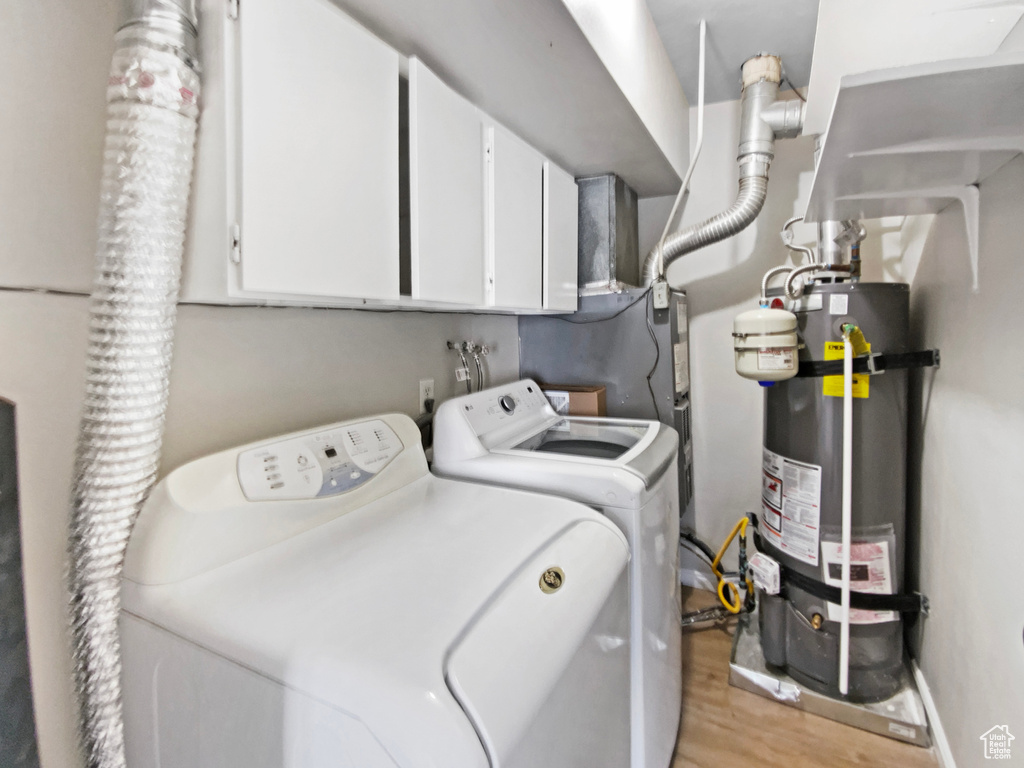 Washroom with washer and clothes dryer, cabinet space, water heater, and light wood-style floors