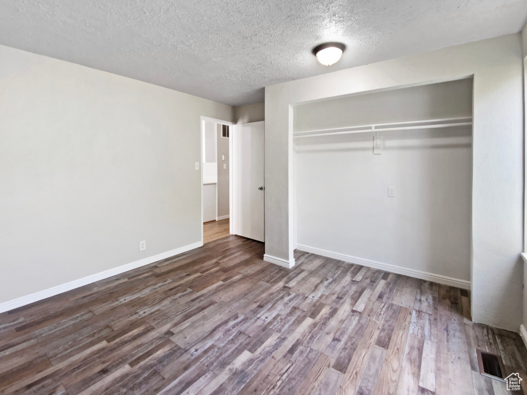 Unfurnished bedroom featuring wood finished floors, a textured ceiling, a closet, and baseboards