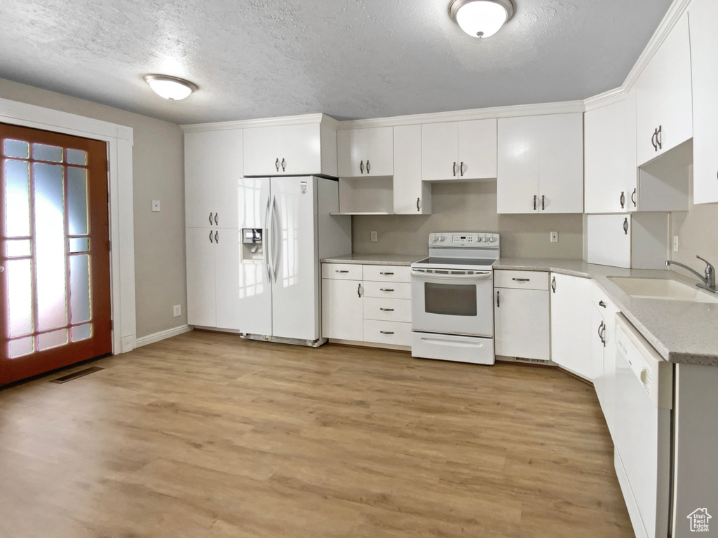 Kitchen featuring white appliances, a sink, a textured ceiling, light countertops, and light wood-type flooring
