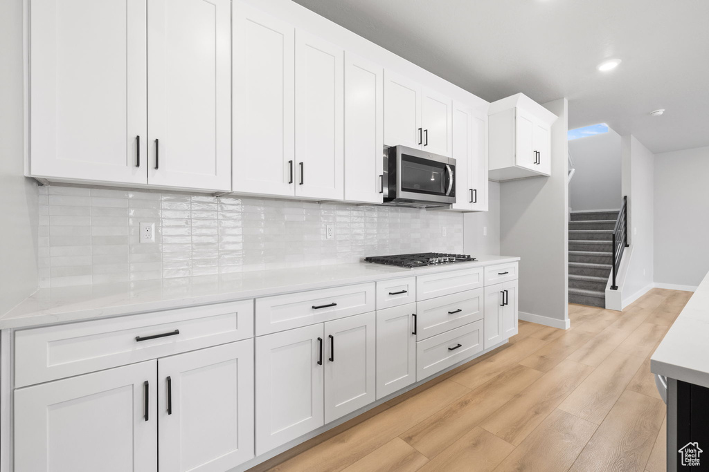 Kitchen featuring stainless steel microwave, white cabinetry, light wood-style floors, light countertops, and recessed lighting