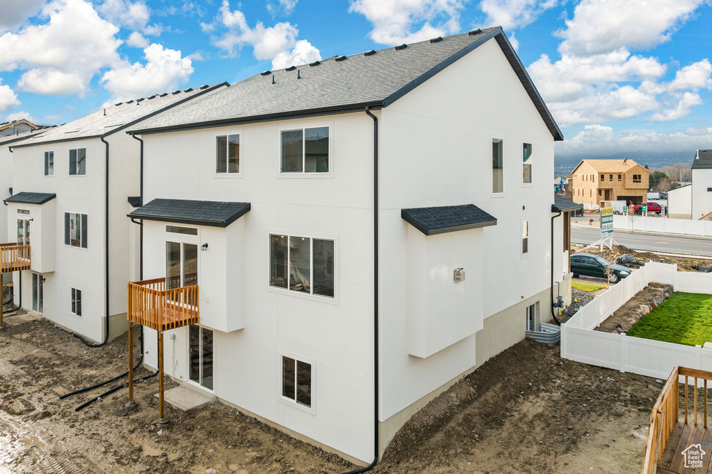 Back of house featuring stucco siding, fence, roof with shingles, and a residential view