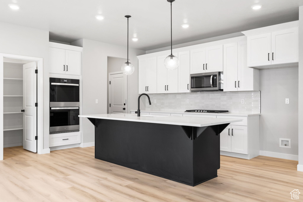 Kitchen with stainless steel appliances, a sink, light wood-style floors, decorative backsplash, and baseboards