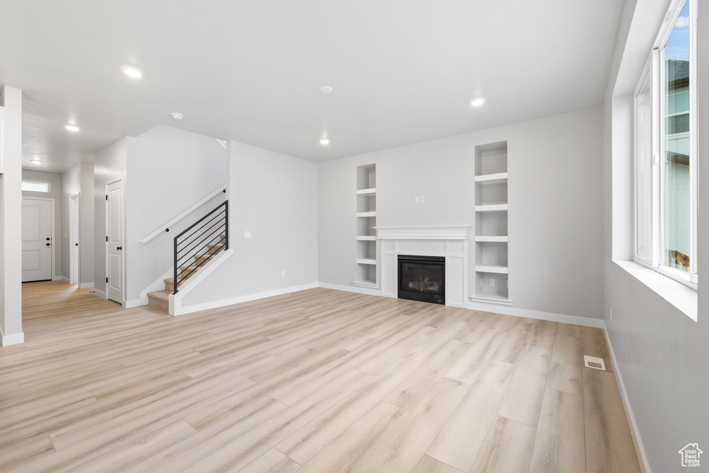 Unfurnished living room featuring baseboards, recessed lighting, stairs, light wood-style floors, and built in features