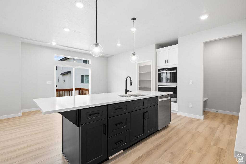Kitchen with a sink, stainless steel dishwasher, multiple ovens, light wood finished floors, and light countertops