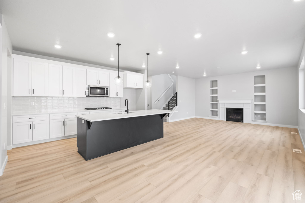 Kitchen featuring stainless steel microwave, a sink, white cabinetry, baseboards, and recessed lighting