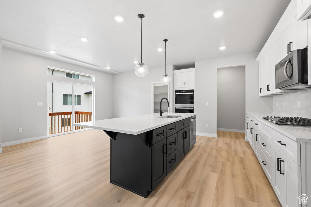 Kitchen featuring stainless steel appliances, a sink, light countertops, dark cabinets, and white cabinets