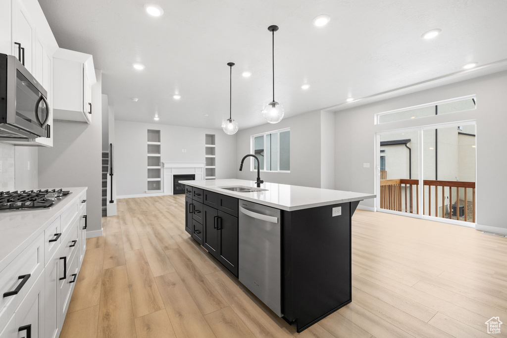 Kitchen with appliances with stainless steel finishes, a sink, light countertops, dark cabinets, and light wood-style flooring