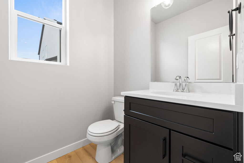 Half bathroom featuring wood finished floors, vanity, toilet, and baseboards