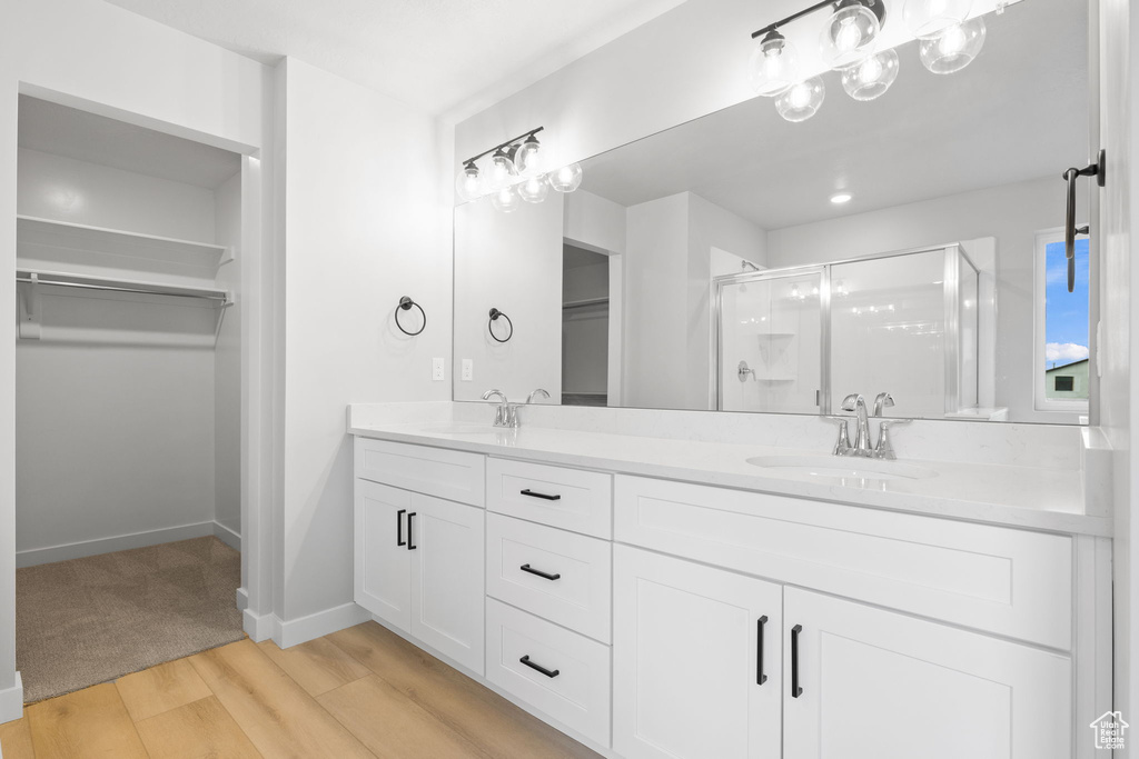 Full bath featuring a shower stall, a spacious closet, double vanity, and wood finished floors