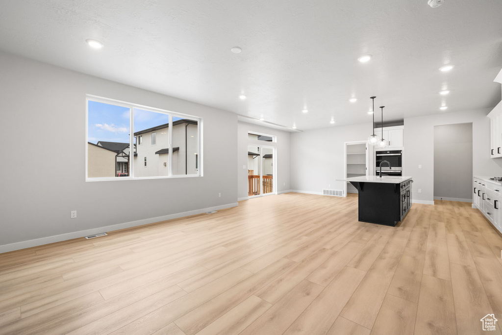 Kitchen with an island with sink, light wood finished floors, light countertops, open floor plan, and white cabinets