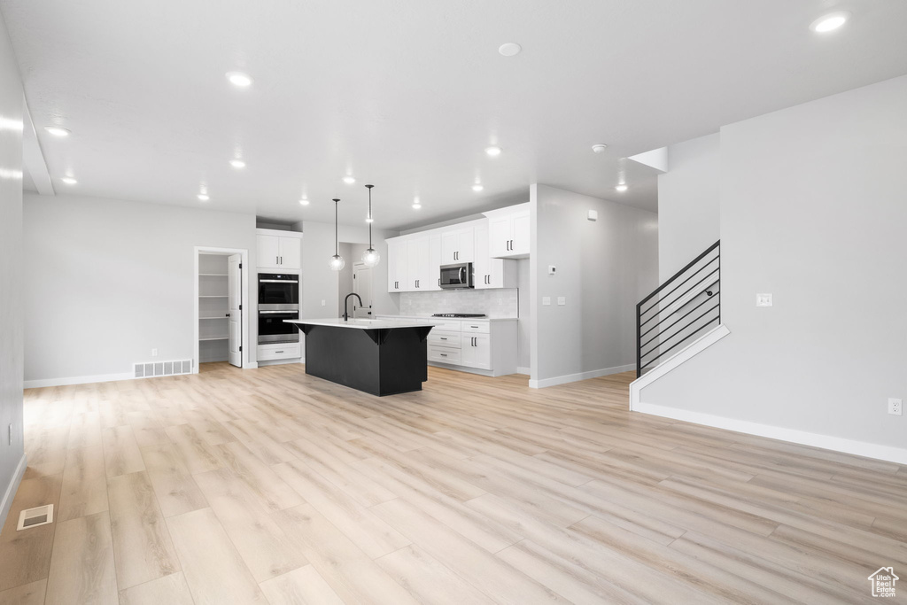 Kitchen with stainless steel appliances, open floor plan, a center island with sink, recessed lighting, and white cabinets