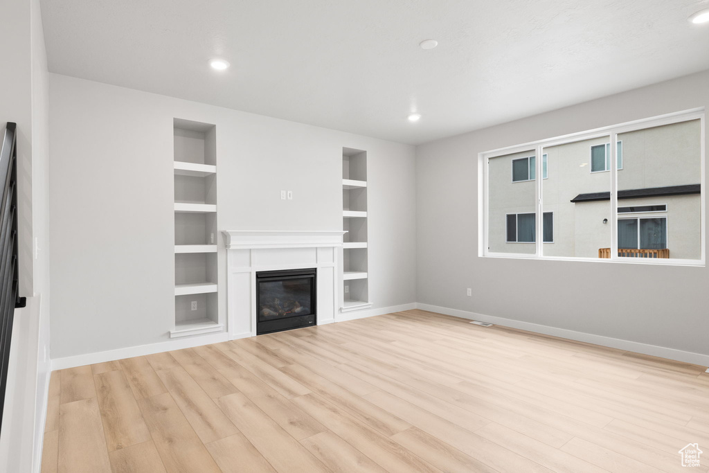 Unfurnished living room with wood finished floors, built in shelves, baseboards, a glass covered fireplace, and recessed lighting