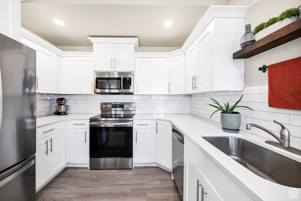 Kitchen with appliances with stainless steel finishes, a sink, light countertops, white cabinetry, and recessed lighting